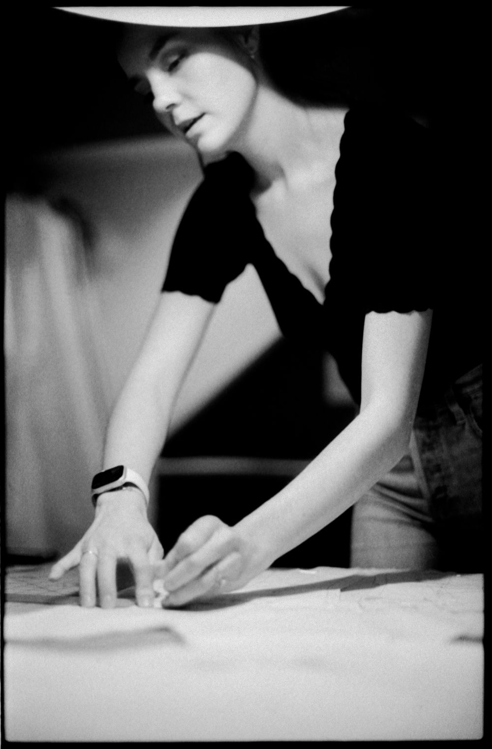 A focused woman in a black top smooths white fabric on a work table wearing a watch in black and white.