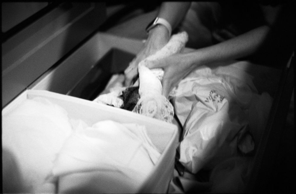Close-up black and white photo of hands carefully handling delicate white fabric from a storage box.