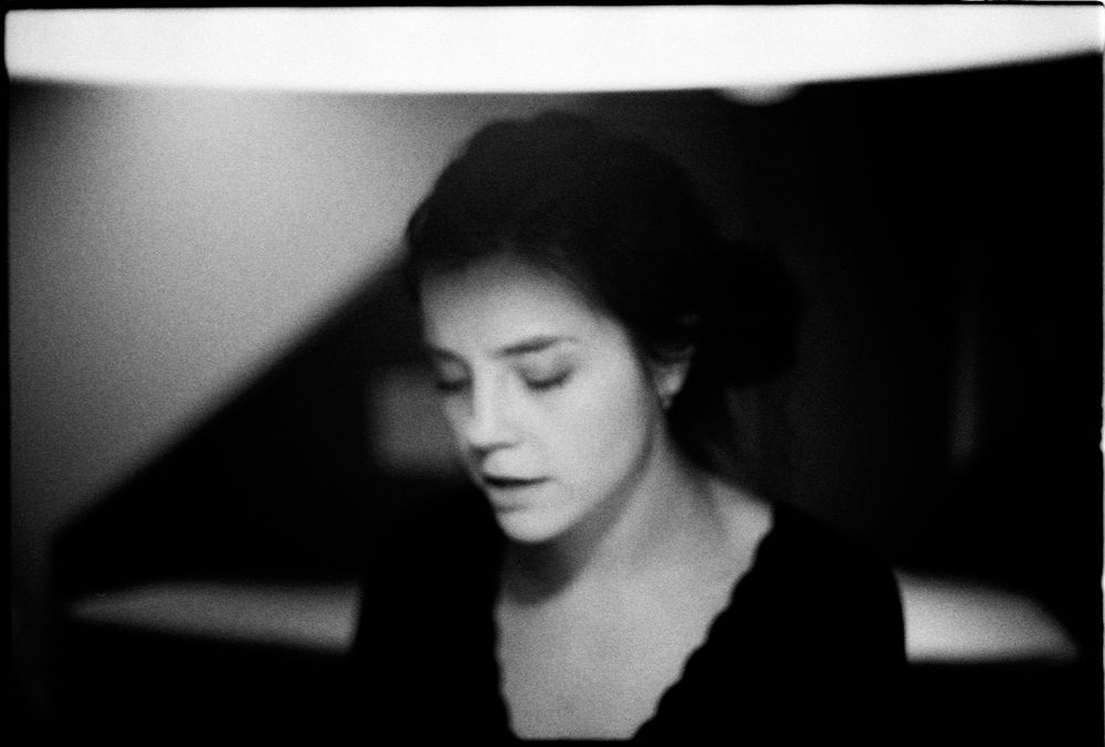 Dramatic black and white portrait of a dark-haired woman in a black top with soft moody lighting.