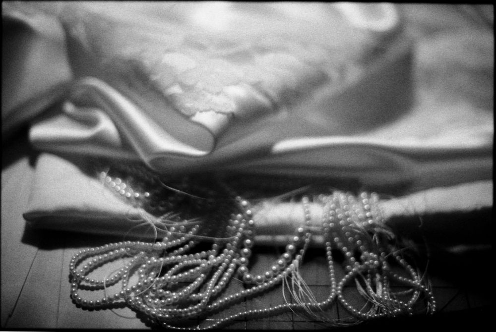 Black and white close-up of elegant white satin fabric and strands of pearl beads on a wooden floor.