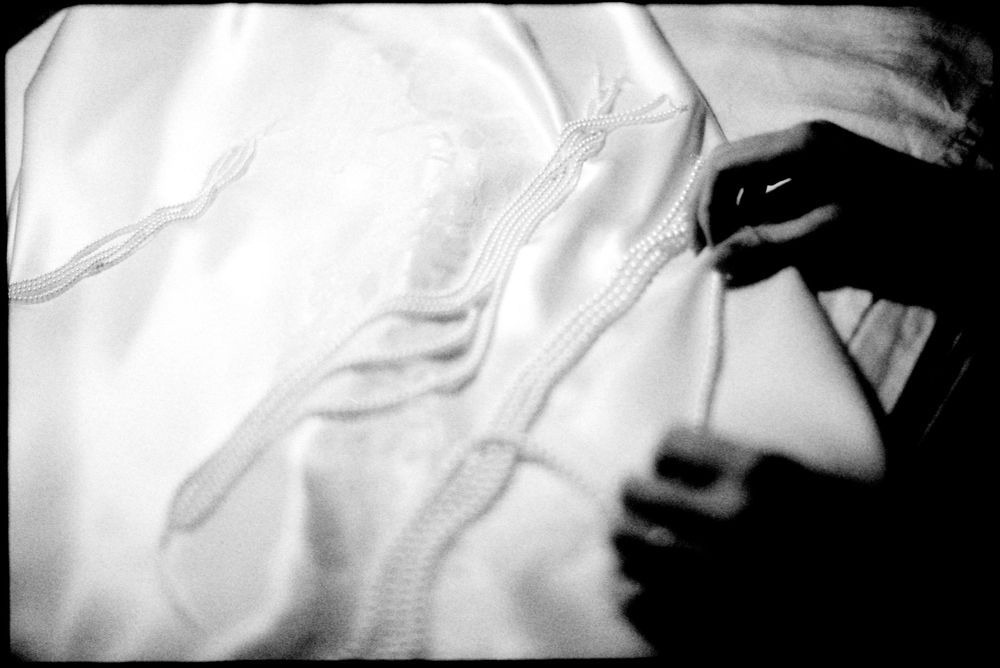 Black and white close-up of hands carefully sewing delicate embroidery on white fabric.