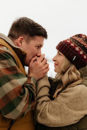 A romantic winter photoshoot showing a couple in cozy sweaters and knit hats sharing intimate moments together.