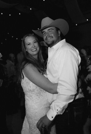 A black and white photo of a couple dancing at a wedding reception, with the groom wearing a cowboy hat and white shirt.