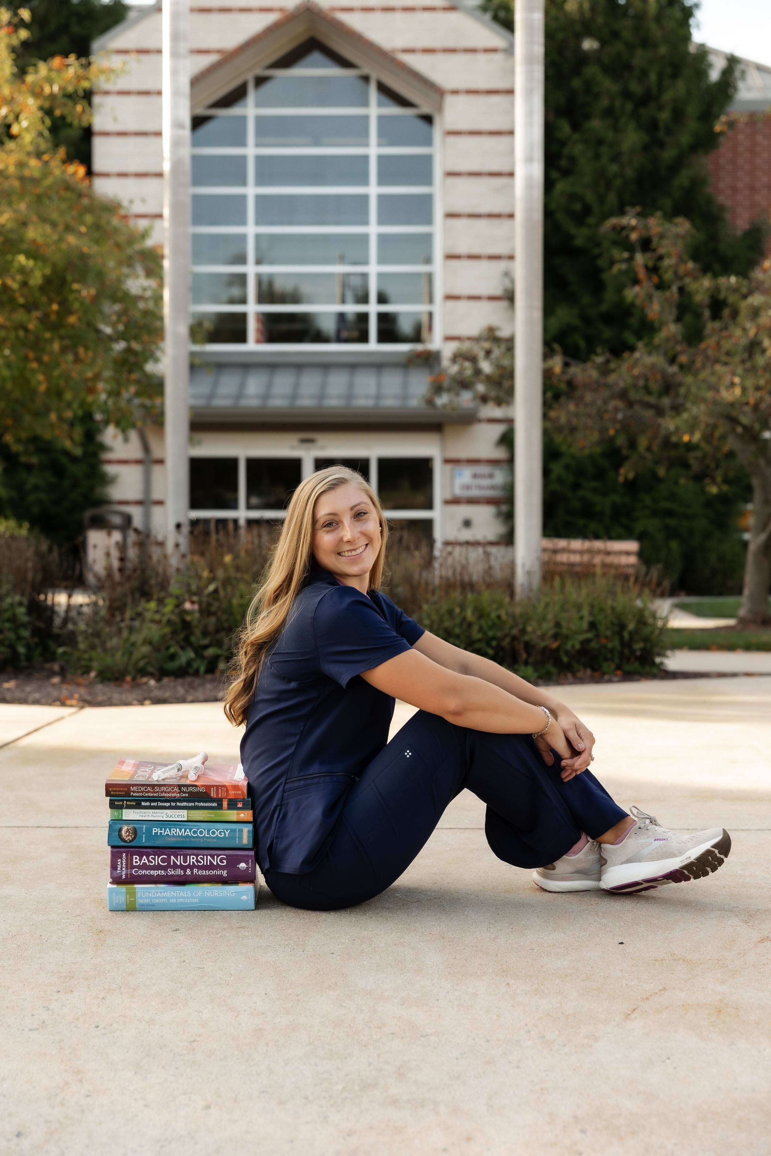 Student sits on ground with textbooks outside a brick building.