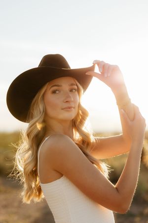 A person in a brown hat poses outdoors during golden hour sunset with sunlight creating a warm backlit glow.