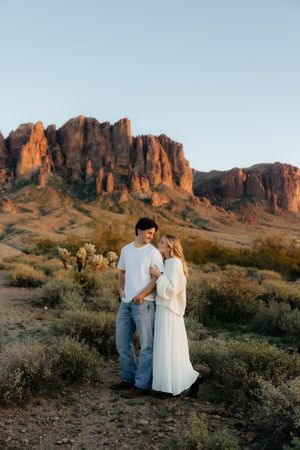 A couple poses together at sunset against the dramatic backdrop of red desert cliffs in the Superstition Mountains.