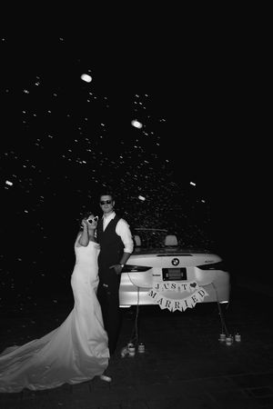 Newlywed couple posing in front of a BMW Just Married car at night in a black and white wedding photo.
