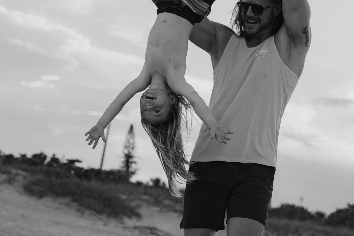 A family plays and jumps together on a sunny beach, wearing coordinated beige and white outfits.