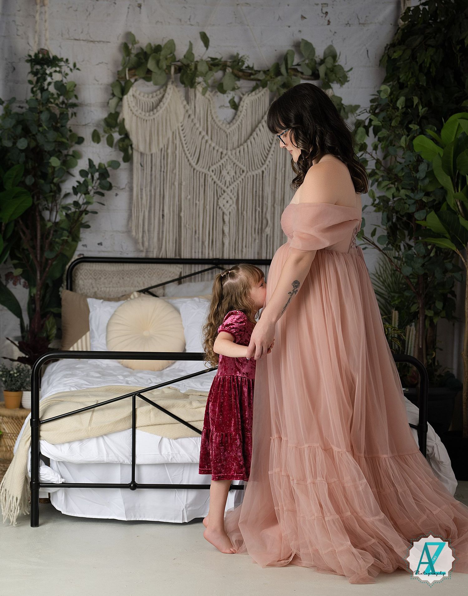 Burgundy and blush gowns displayed in studio setting with macrame wall art and climbing vine decorations.