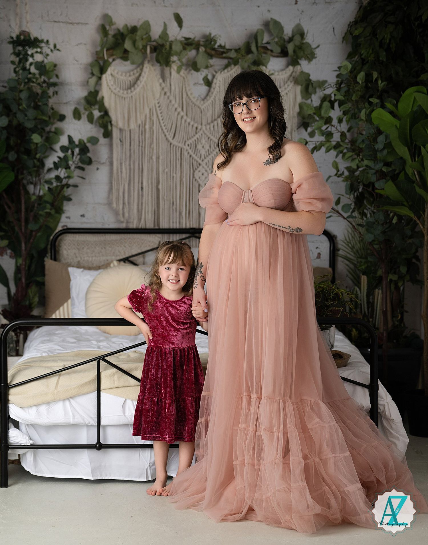 A sweet indoor portrait featuring matching pink and burgundy dresses against a decorated macrame backdrop.