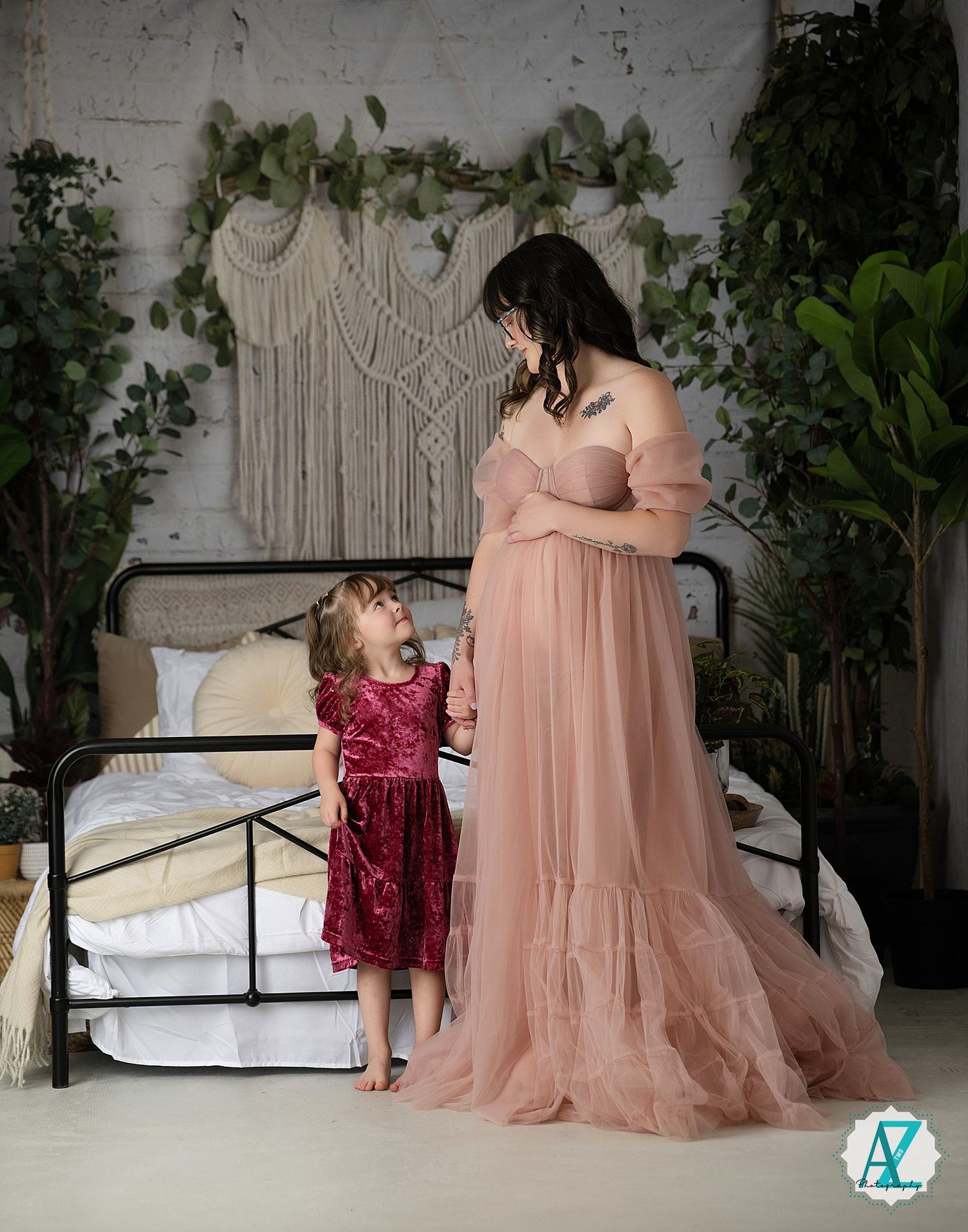 A series of romantic maternity photos showing a burgundy dress and peach gown against a rustic white backdrop with greenery.