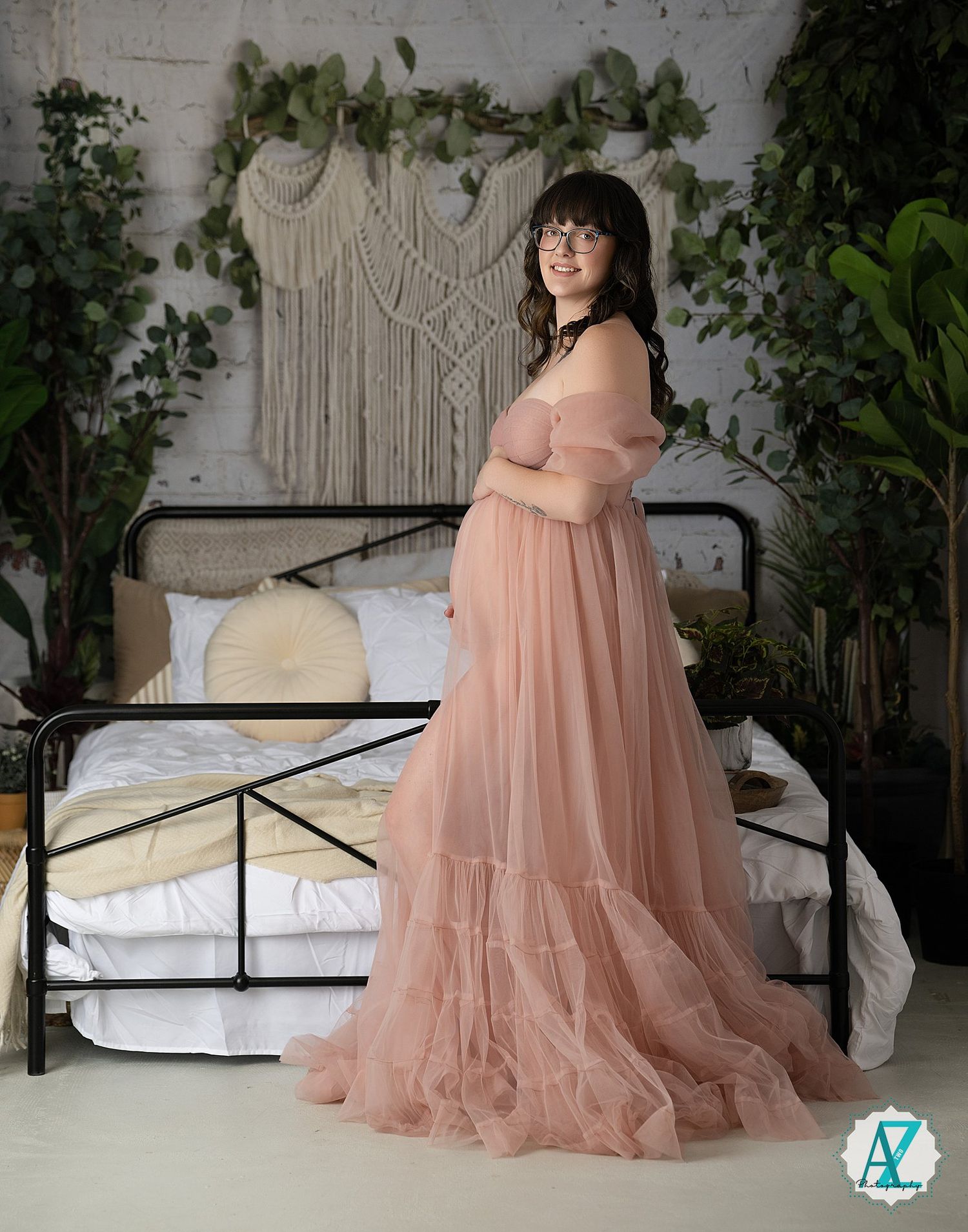 A flowing peach tulle maternity gown is showcased in a bedroom setting with macrame wall art and greenery.