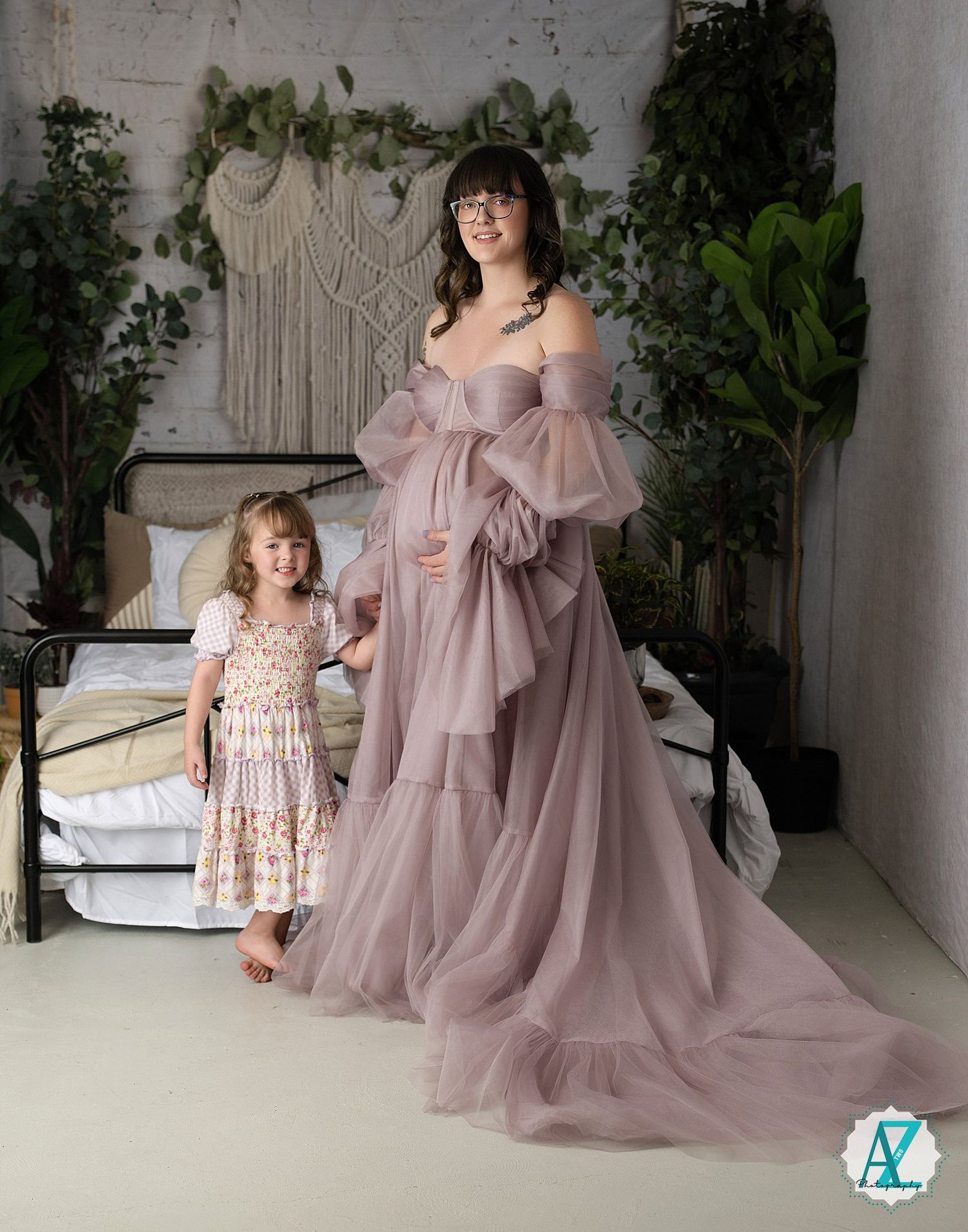 A group poses in flowing mauve tulle dresses against a white studio backdrop with greenery decor.