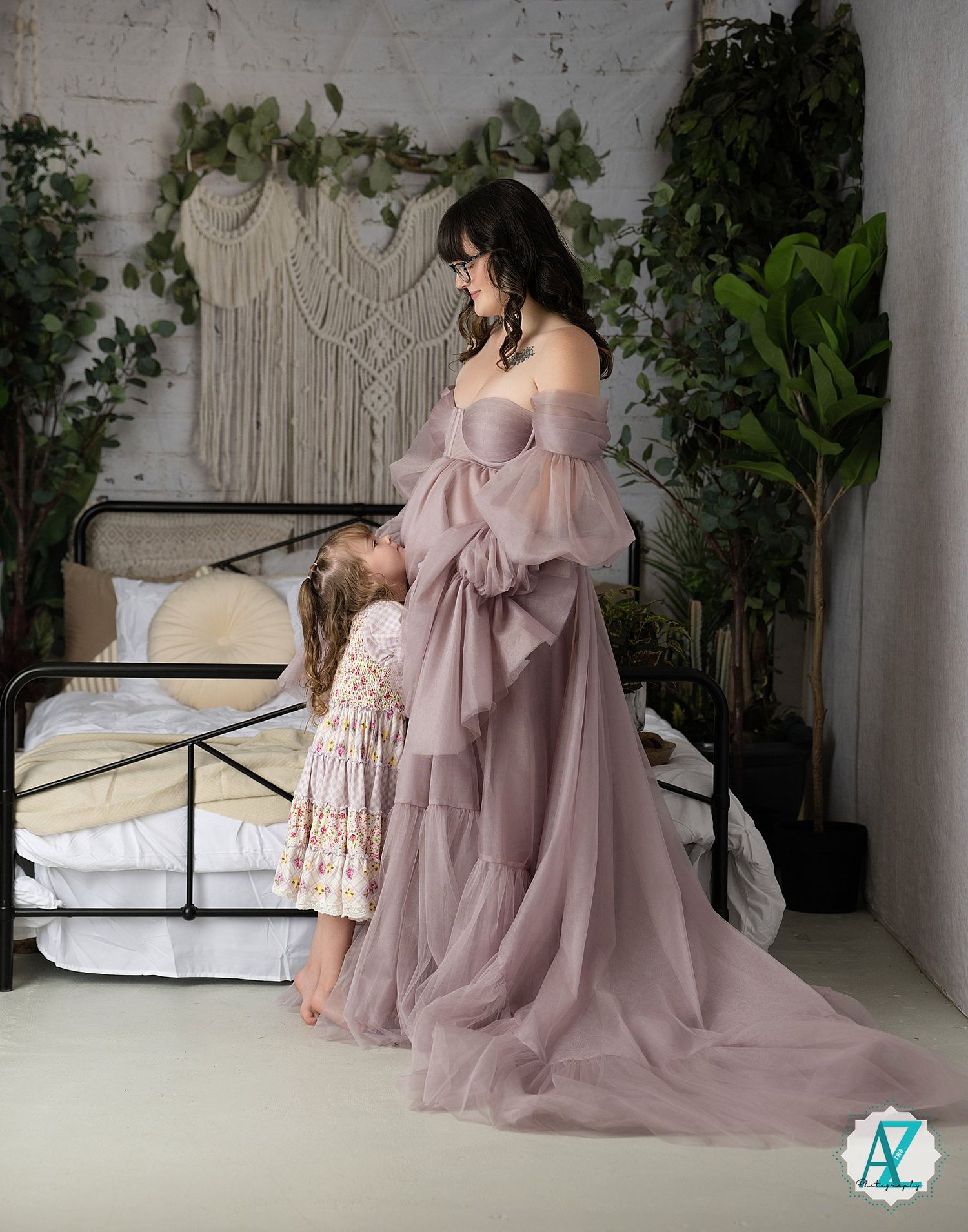 Two people in coordinating dusty rose and floral outfits pose together on a white backdrop with greenery accents.