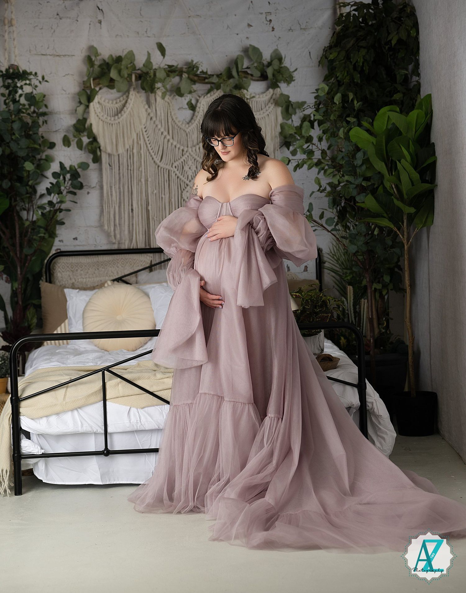 A dreamy maternity photo featuring a flowing dusty rose tulle gown against a macrame backdrop with greenery.