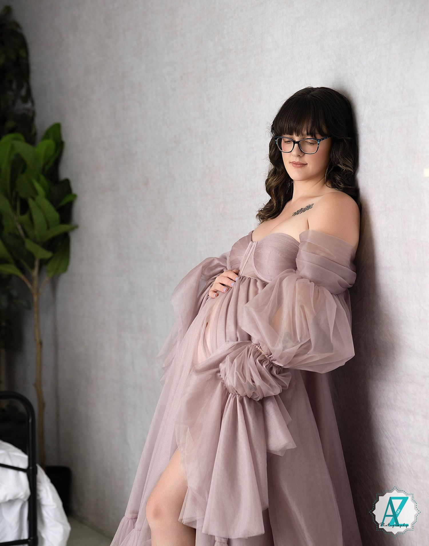 Woman in a flowing blush pink dress poses against a white wall with indoor plants.