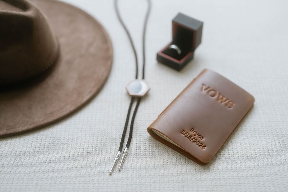 Brown leather accessories and wedding details arranged on a light colored surface.