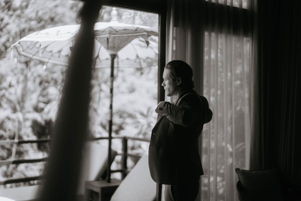 Silhouetted figures stand near windows in a dimly lit interior space.