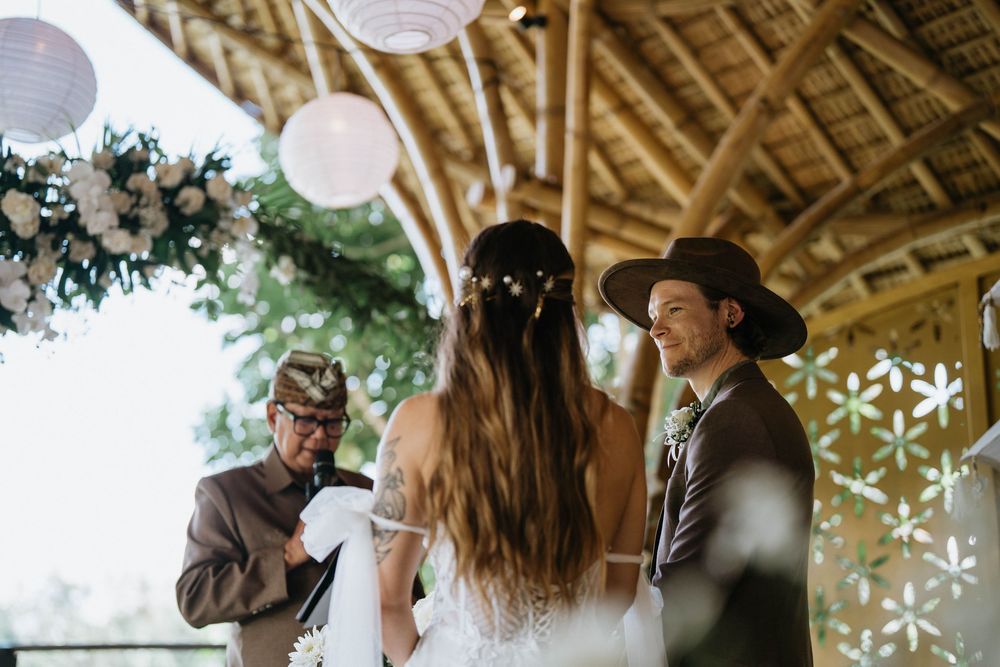 A romantic wedding ceremony takes place under a rustic wooden pavilion decorated with white lanterns and floral arrangements.