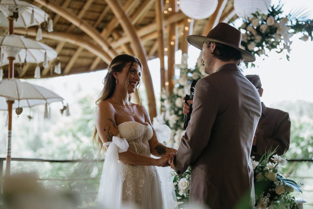 Intimate wedding moment captured under a wooden structure with decorative white lanterns and greenery.