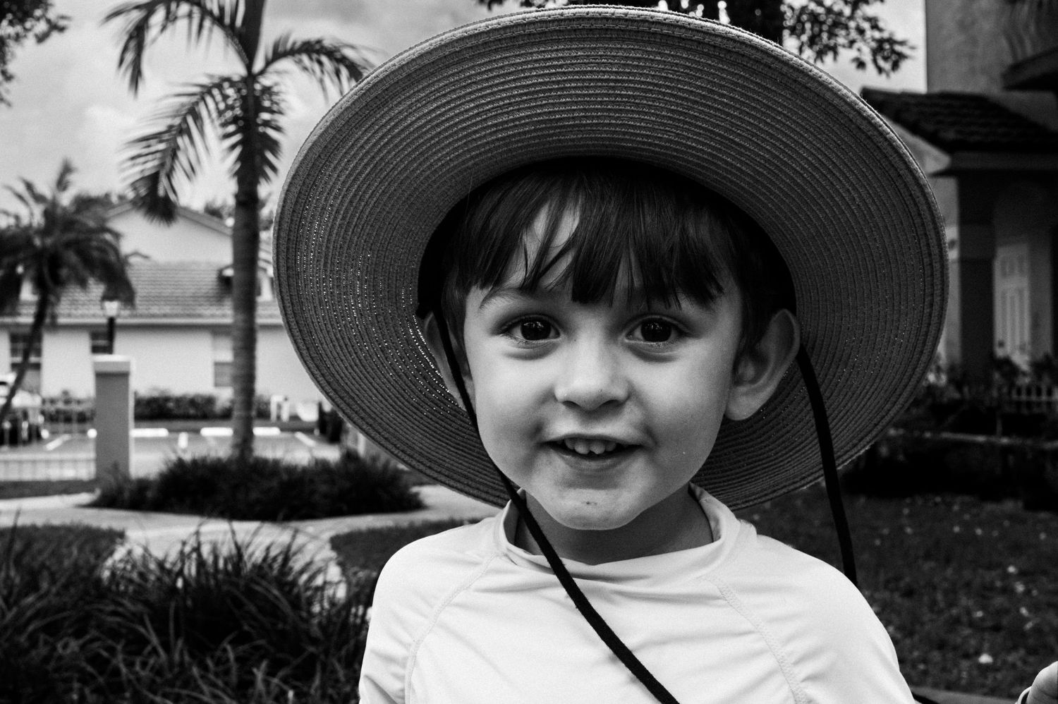 A collection of five black and white portrait photos showing a young child wearing a wide-brimmed hat outdoors.