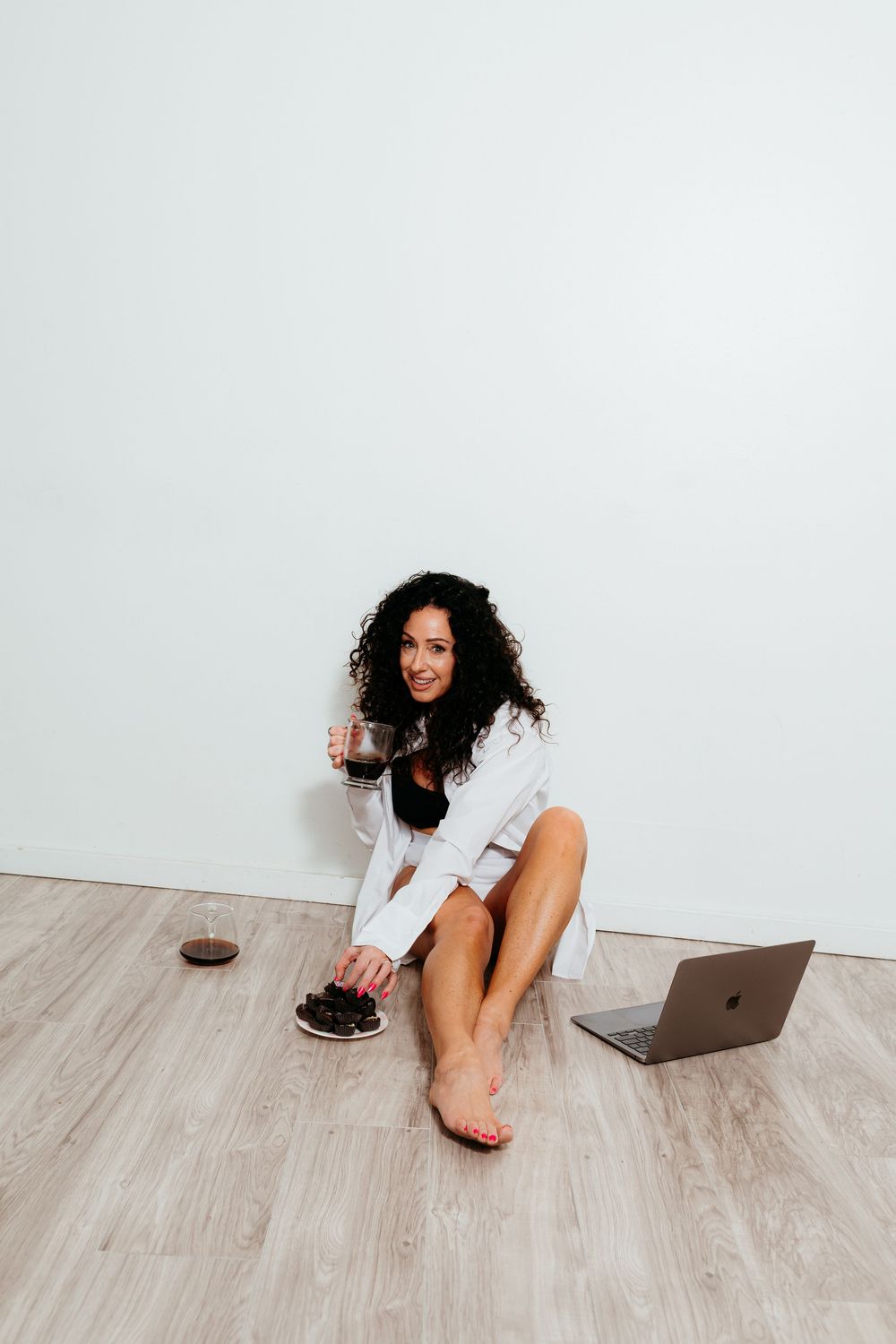 Person in white shirt relaxes on wooden floor with laptop and snacks.