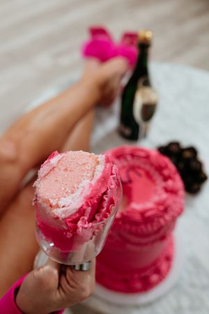 Close up of pink birthday cake being served with champagne and chocolates nearby.