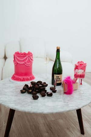 A minimalist display of pink cake, chocolate truffles and champagne bottle on marble surface.