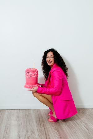 Someone in vibrant pink attire presents a beautifully decorated pink cake against a minimalist white background.