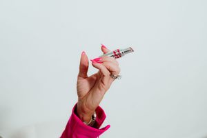 Hand in pink sleeve holding lipstick against white background.