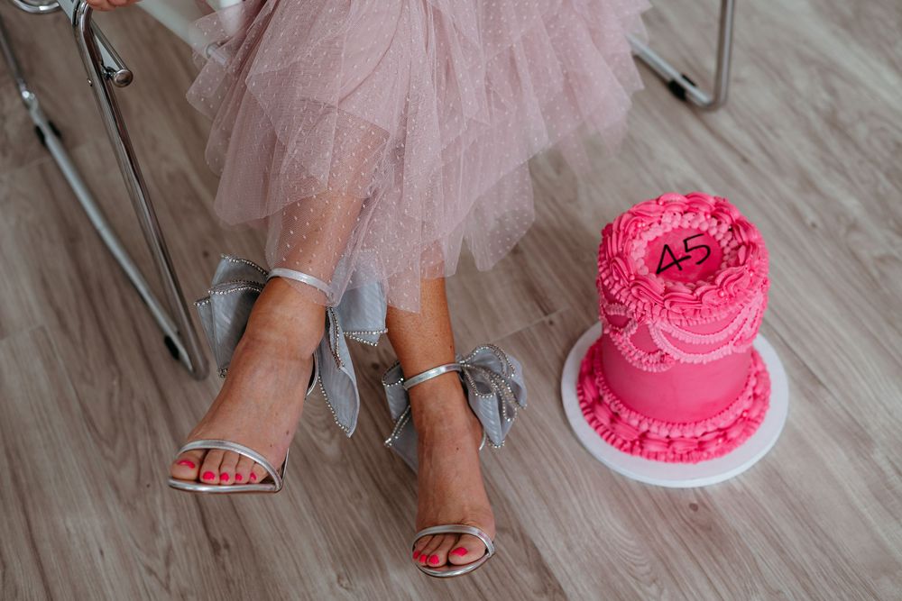 A person in a pink tulle skirt sits on a modern chair next to a vibrant pink frosted cake.