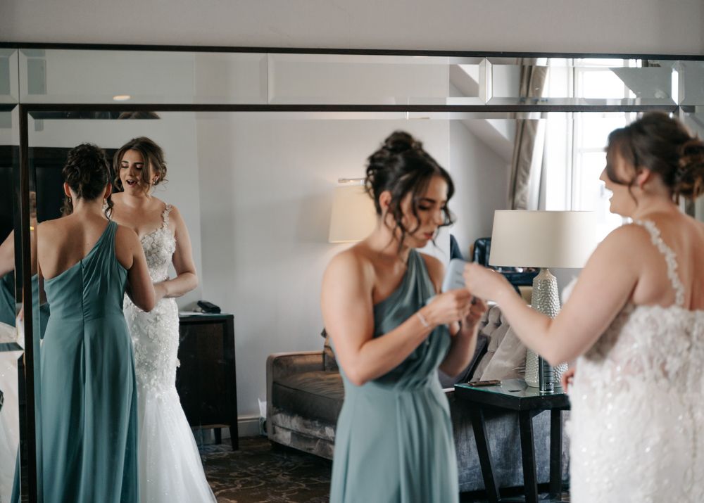 Bridesmaids in teal dresses helping with final wedding dress adjustments.