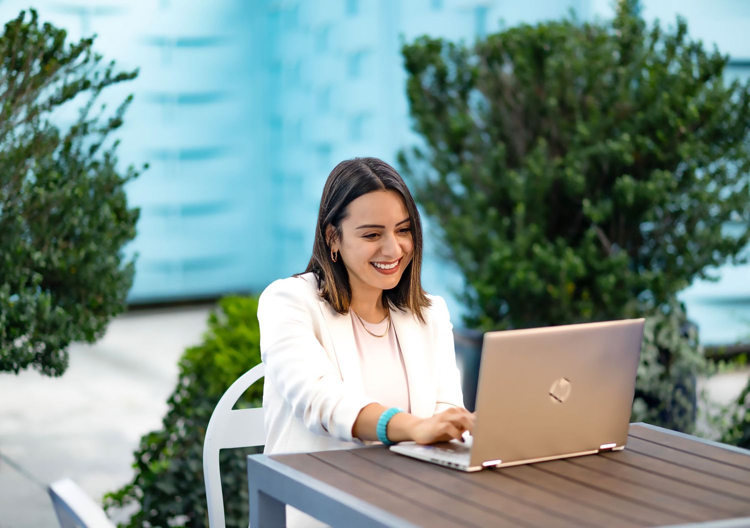 A person works on a laptop at an outdoor desk with lush green foliage in the background.