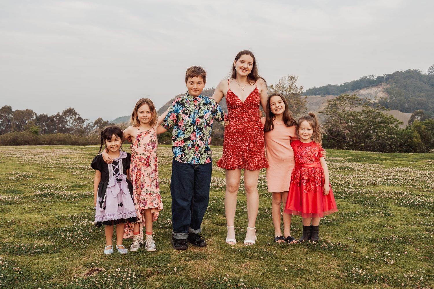 A group of people in colorful dresses and shirts pose together on a grassy hillside on an overcast day.