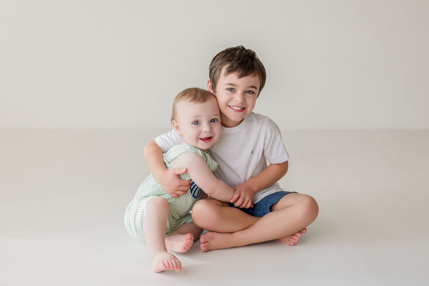 Two people lying on white backdrop during lifestyle portrait session, smiling and looking up at camera.