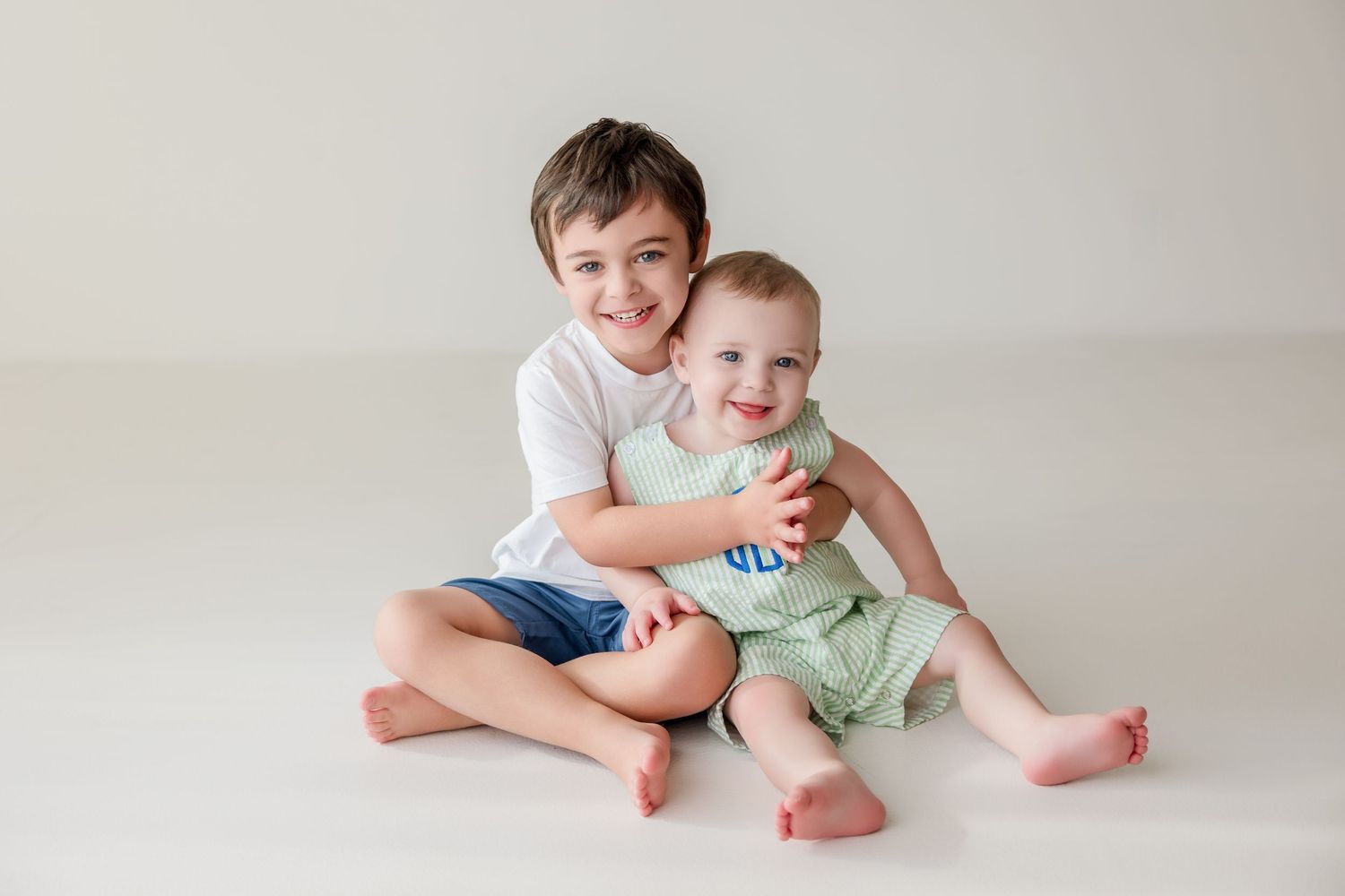 Kids in casual clothing sit together on white background in studio setting while smiling and playing.