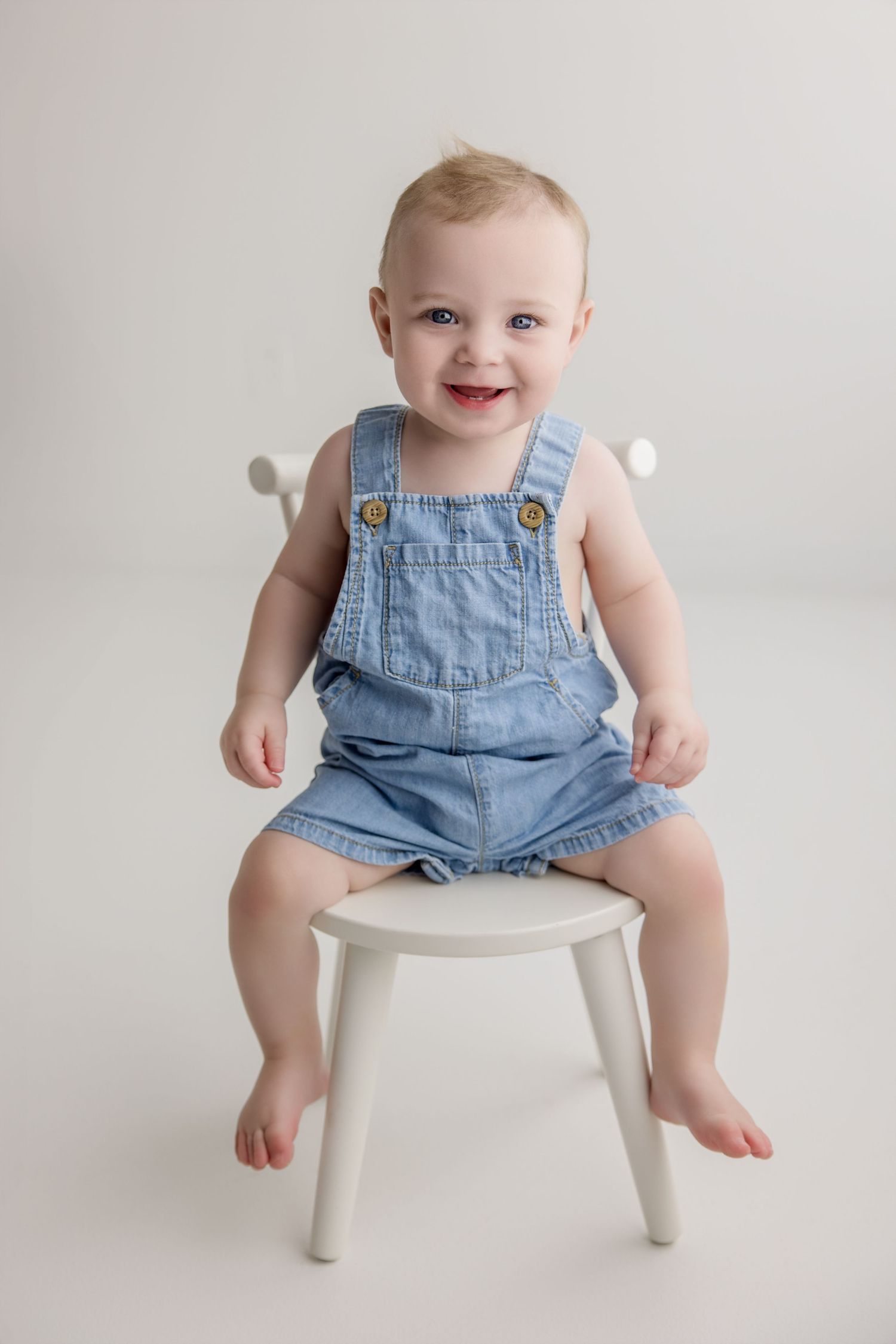 Little one sits on a white stool wearing blue denim overalls against a light backdrop in a progression of images.