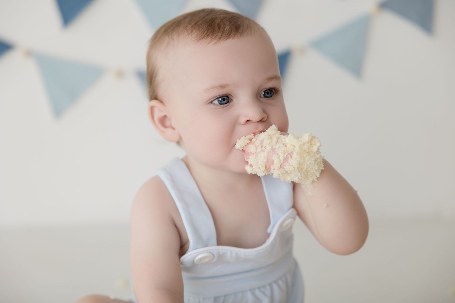 Small child holding white cookies while sitting against a bunting banner background.