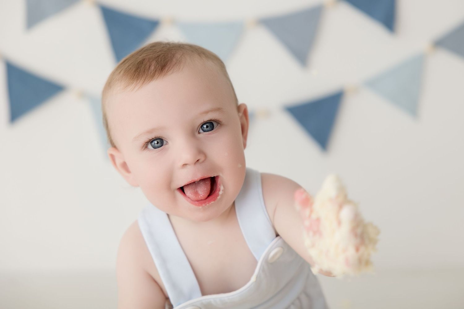 Baby sitting in front of blue and white pennant banner background during first birthday cake smash session.