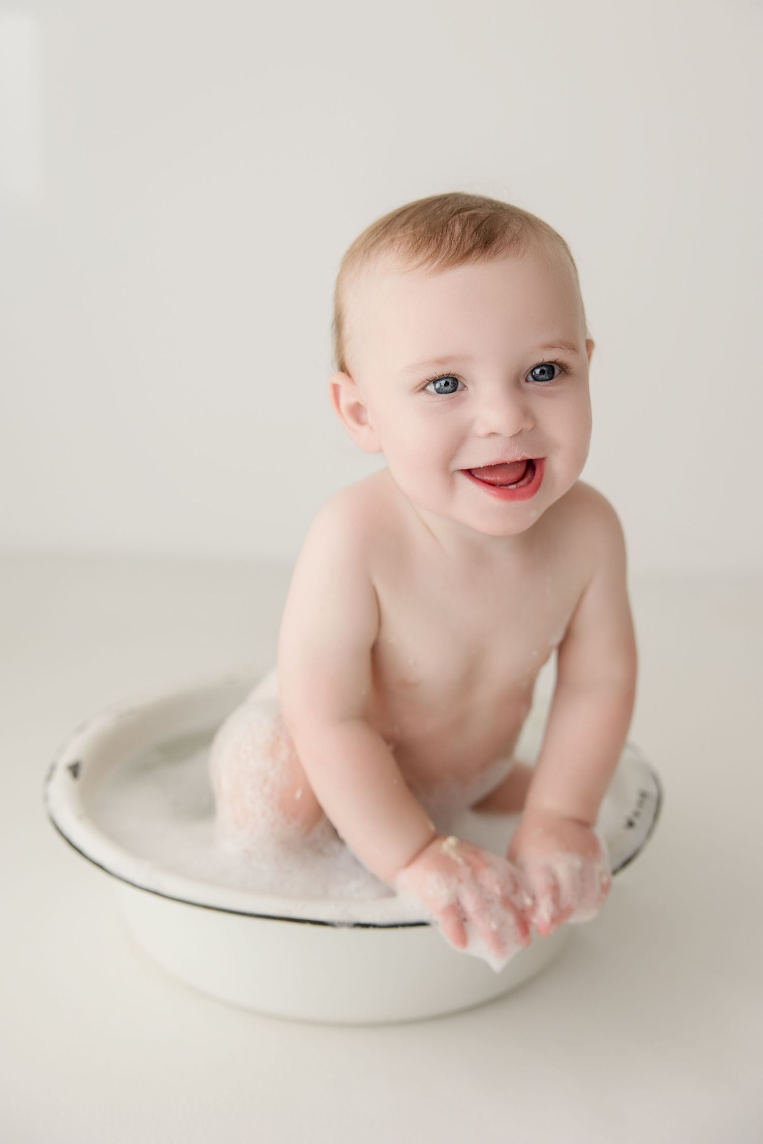 Baby lying on white backdrop during professional photo session with joyful expression.