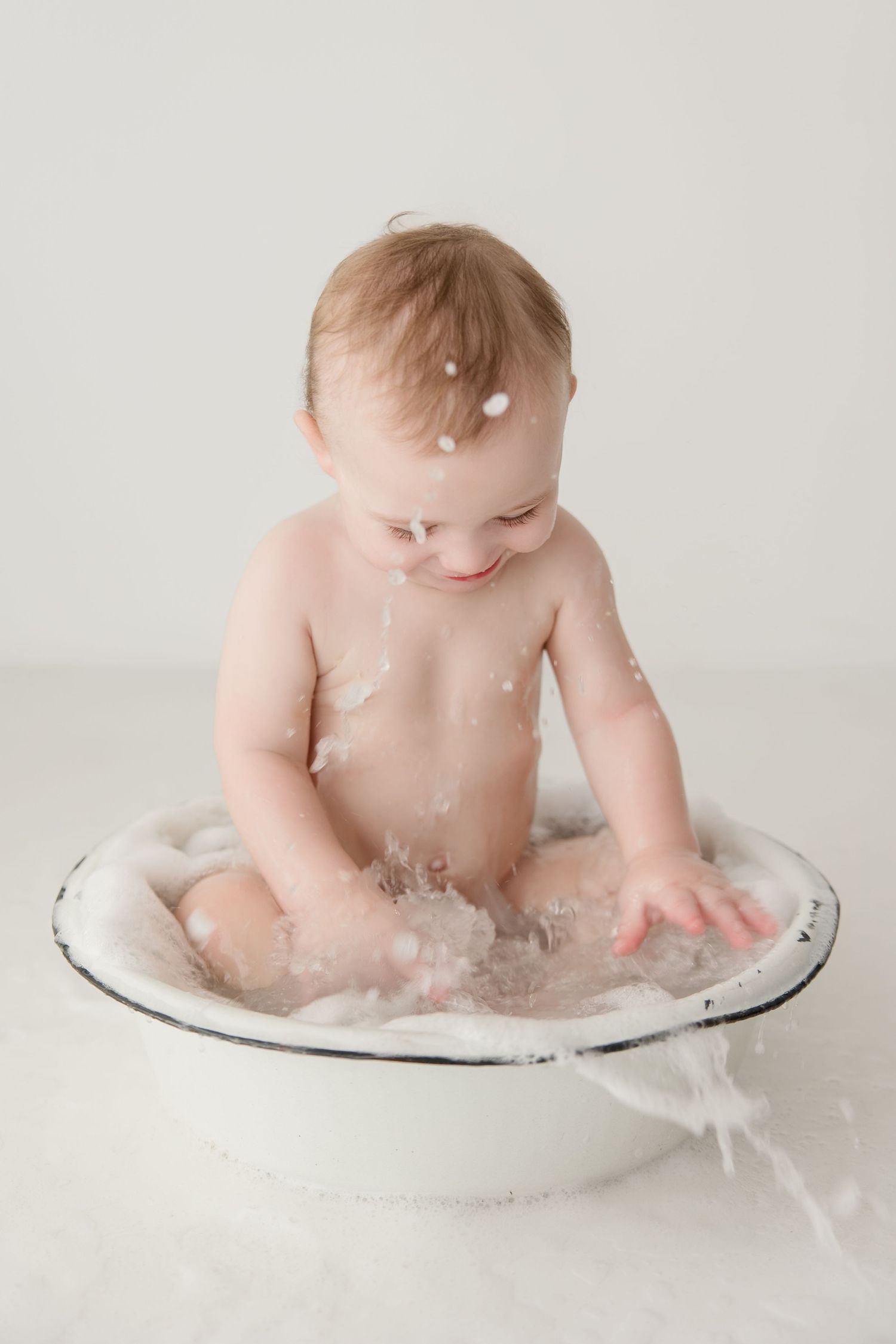 Joyful baby splashes and plays in a vintage metal bowl with feathers.