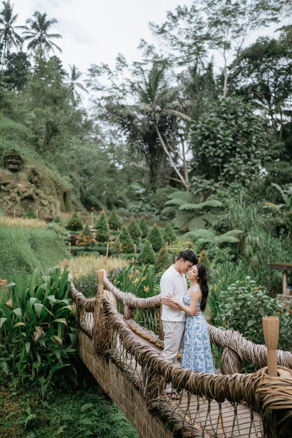 A tender moment shared on a rustic rope bridge surrounded by tropical plants.