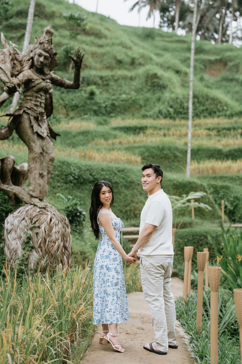 A scenic pathway winds through tropical landscaping with gnarled trees and bamboo fencing.