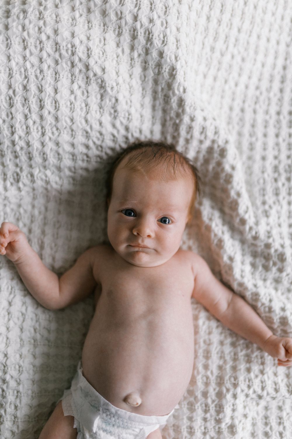A newborn baby lying on a textured white blanket, wearing only a diaper.