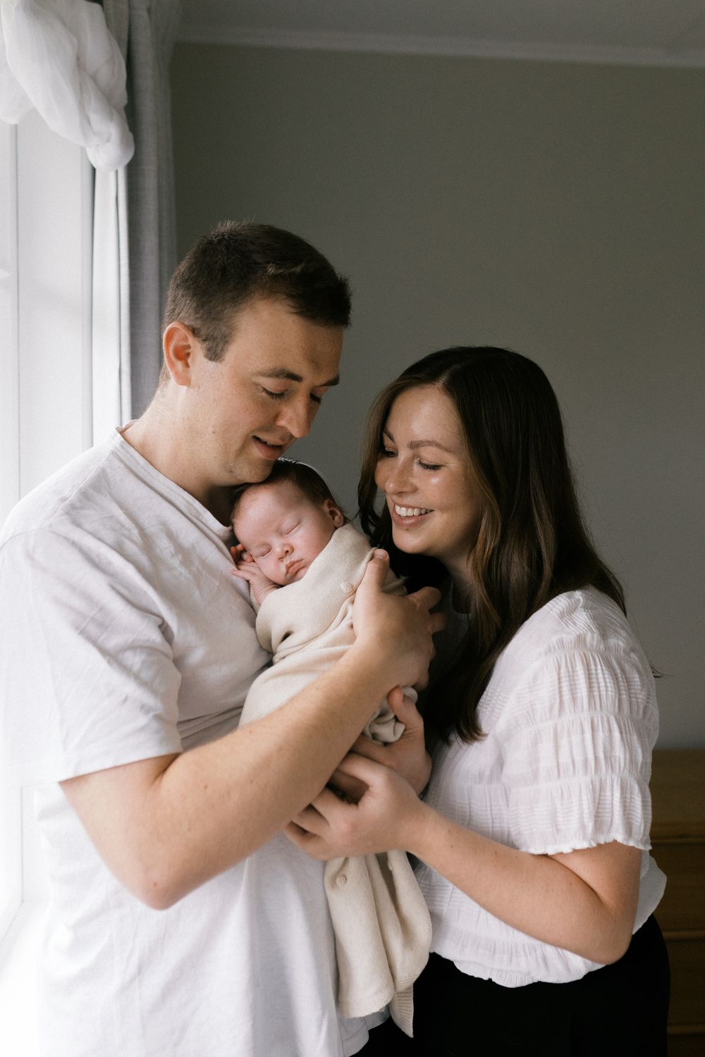 A series of four intimate black and white family photos showing tender moments with a newborn baby against a white backdrop.