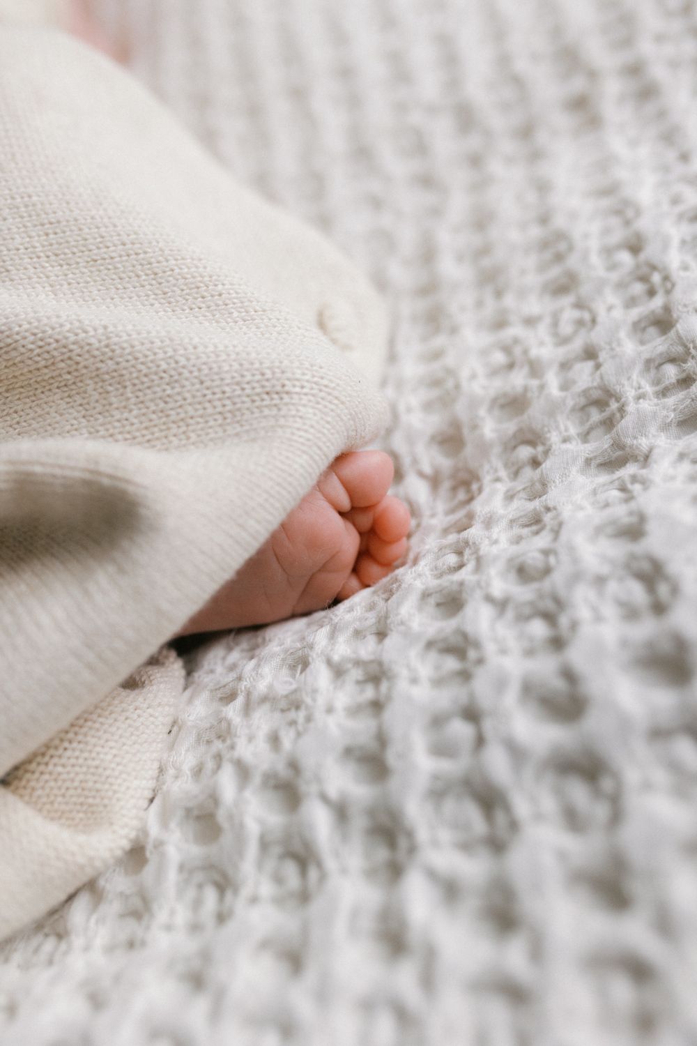 Close-up shots of tiny baby feet peeking out from under a white knitted blanket.