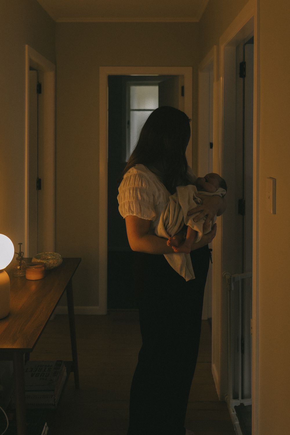 Silhouette of person holding baby in dark hallway with warm ambient lighting.