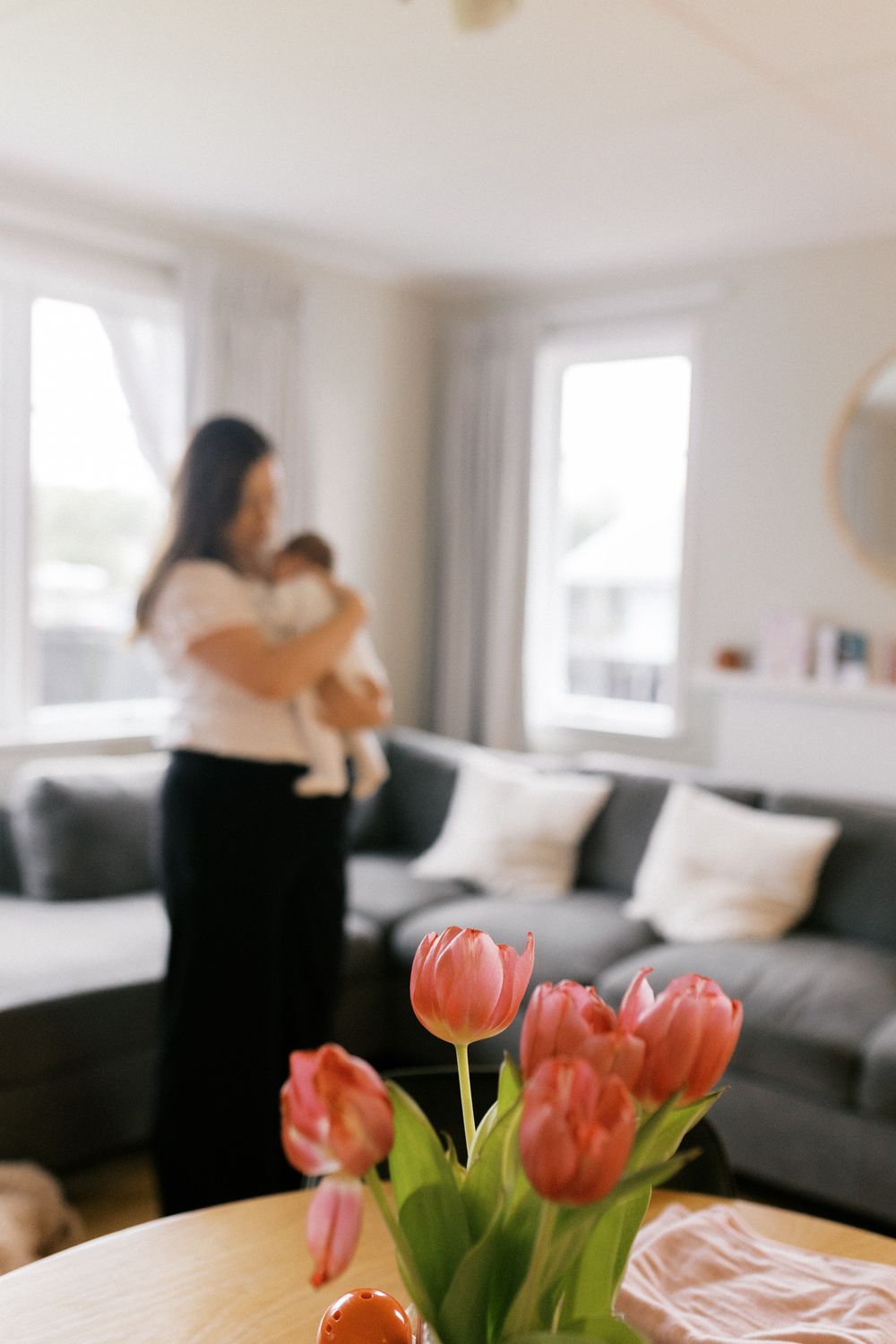 Living room scene with pink tulips in foreground and blurred figures interacting in background.