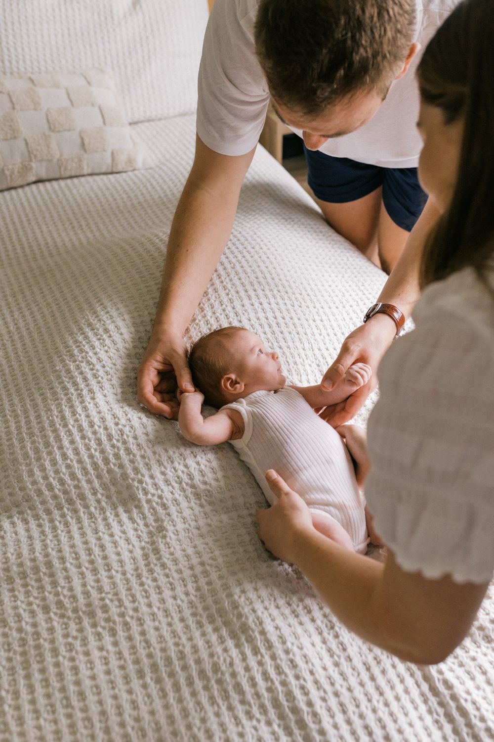 Caregivers leaning over a bed while tending to a baby on a textured white surface.