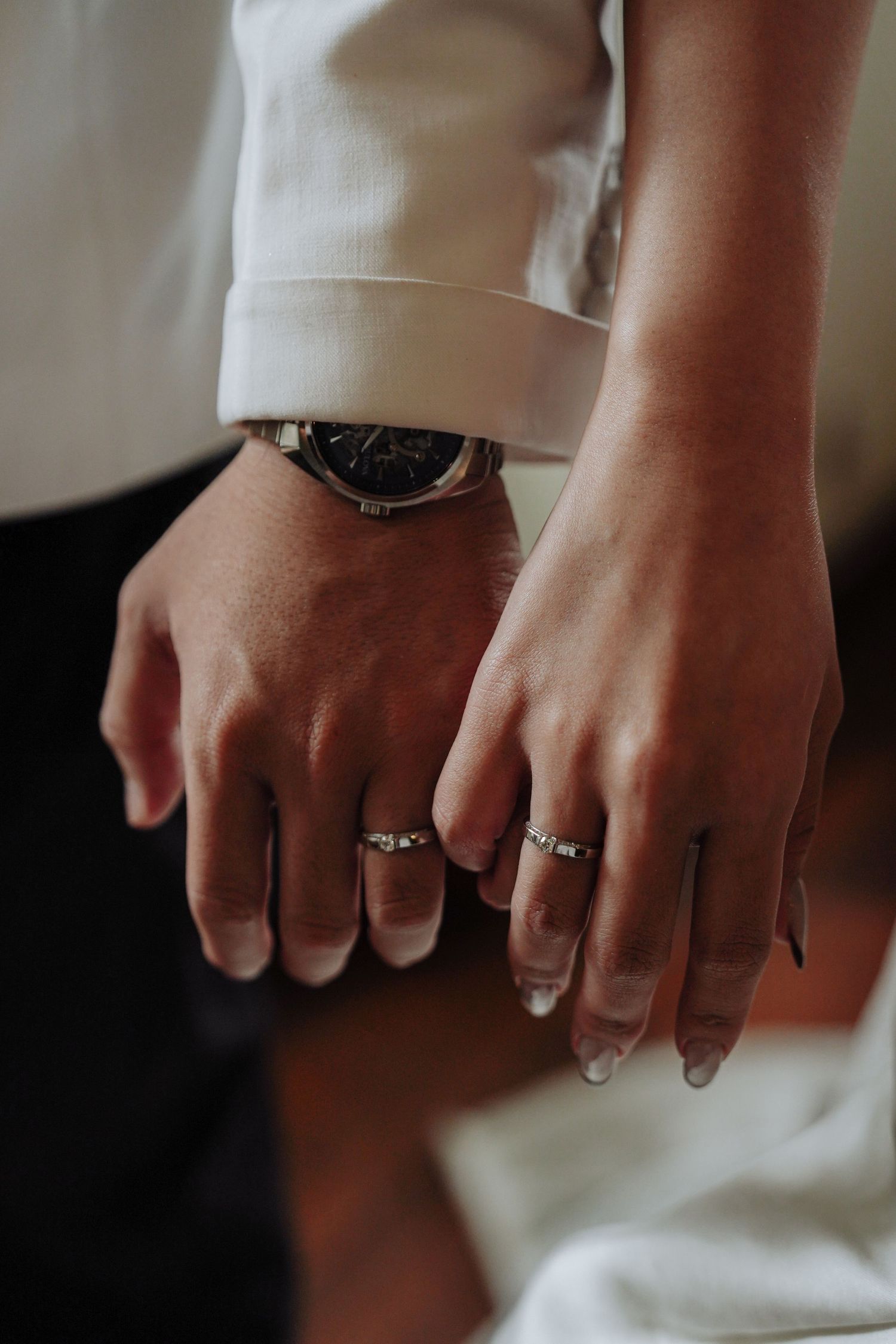 Close-up of newlywed couple's hands showing matching wedding rings, with groom wearing a classic wristwatch.